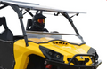 A rider in black motocross gear and red-tinted goggles sits inside a yellow vehicle equipped with a Can-Am Commander Scratch Resistant Flip Windshield (2011-2020), featuring a roll cage, against a plain white background.