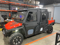 A GC1K Crew Armor Tech Enclosure, a rugged black and red off-road utility vehicle with large tires and an enclosed cabin, is parked in an industrial warehouse with metal shelves, boxes, and tools visible in the background.