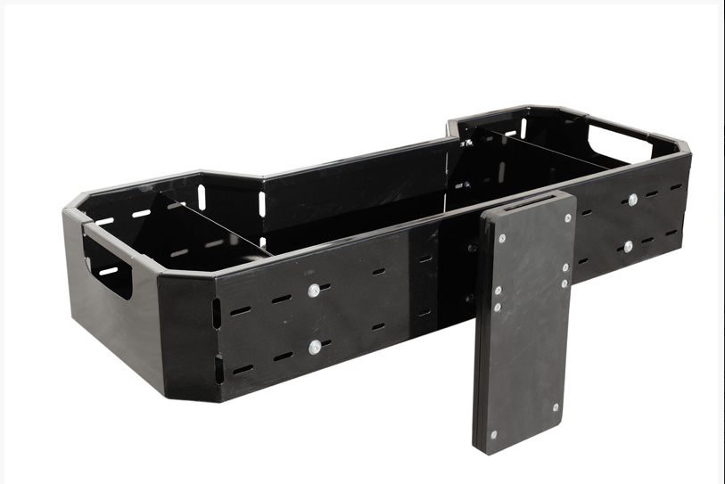 The Universal Cargo Box: + Chainsaw Holder is a black rectangular metal box with slotted side panels, visible bolts, open end handles, and a flat attachment for holding a chainsaw—combining industrial style with robust utility.