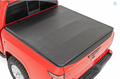 A red Nissan Frontier (22-23) pickup is shown from a rear three-quarter angle on a white background, featuring a smooth, black Soft Tri-Fold Bed Cover securely fastened over the bed for full coverage.