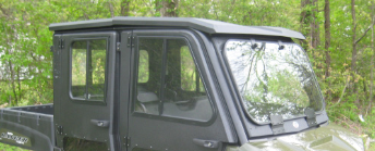 A close-up of a Polaris Ranger 570 SP (2022-PRESENT) with windshield, steel roof, and back panel installed, parked outdoors amid green trees and foliage.