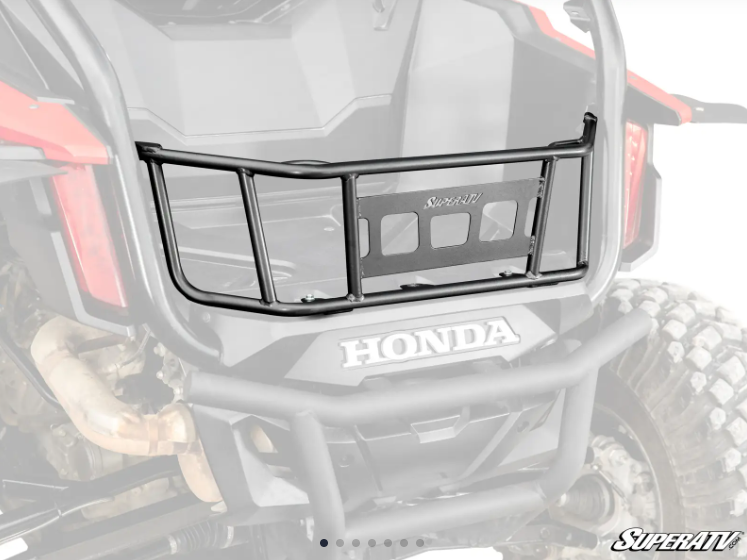 A SuperATV Honda Talon 1000 Bed Enclosure, made of black metal with horizontal and vertical bars and a central rectangular plate, is installed above the rear bumper of a Honda off-road vehicle. The background appears slightly faded.