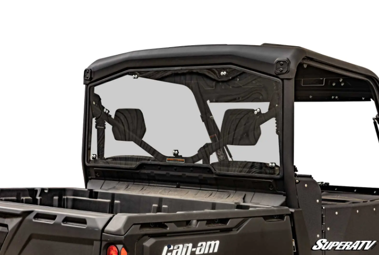 A rear view of a black Can-Am utility vehicle displays the Can-Am Defender Rear Windshield by SuperATV, featuring a clear, vented design with two open vents, black frame, and cargo bed. The SuperATV logo appears in the lower right corner.