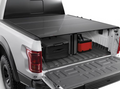 A 2014-18 Chevy Silverado 6ft 6in box is shown with the Alloycover Hard Folding Bed Cover (black) partially open, revealing two black suitcases and a red and black toolbox in the bed; rear tires and taillight are visible.