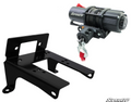 The Canam Commander Winch Mount and 3,500lb Winch set includes a black metal bracket beside a compact electric winch with SuperATV branding, steel cable, red pull strap, and hook. Set against a white background with the logo in the corner.