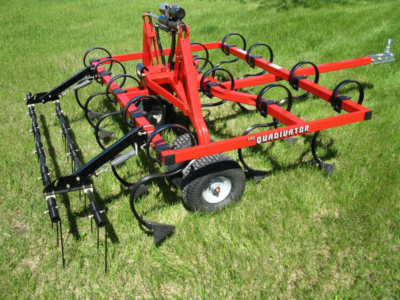 A Universal ATV/UTV Cultivator - Heavy Duty Commercial Grade in red and black sits on green grass, featuring sturdy wheels, curved tines for tilling, and an attachment with vertical rods for aerating or raking.