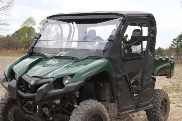 A green Yamaha Viking UTV (2015+) with a black roof, transparent windshield, large rugged tires, open cargo bed, and black Yamaha Viking Full Frame Door Kit is parked on a dirt field. Trees can be seen in the background.