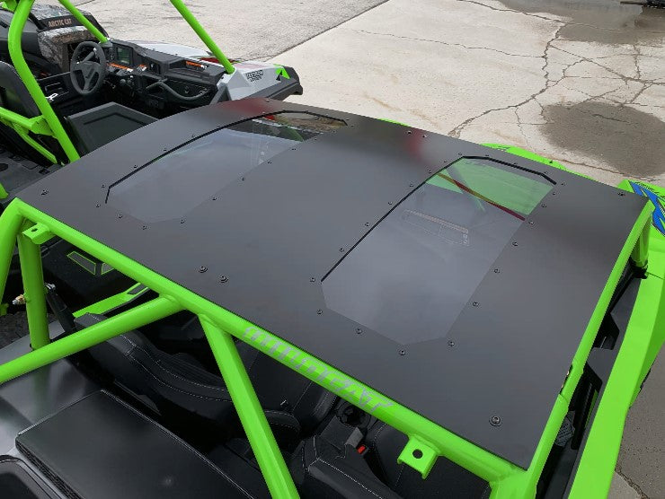 A Wild Cat Xx Aluminum Roof/Top With Sunroof is installed on a bright green off-road vehicle. Two transparent sunroof panels reveal the interior, including steering wheel and seats. The vehicle is parked on cracked concrete.