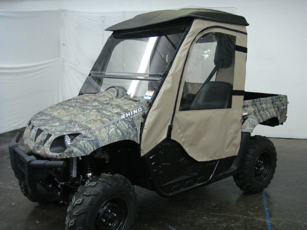 A Yamaha Rhino 450/660/700 (2004-13) fitted with the Soft Door Kit, featuring tan fabric and clear plastic windows, is parked indoors on a concrete floor near white partition walls. The UTV has rugged tires and a camouflage pattern.