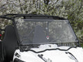 A Yamaha Wolverine R-Spec (2016-2018) with a 1 Pc. Lexan Windshield is parked by blossoming trees. The white off-road vehicle features two black bucket seats, safety harnesses, visible roll bars, and a windshield reflecting outdoor light.