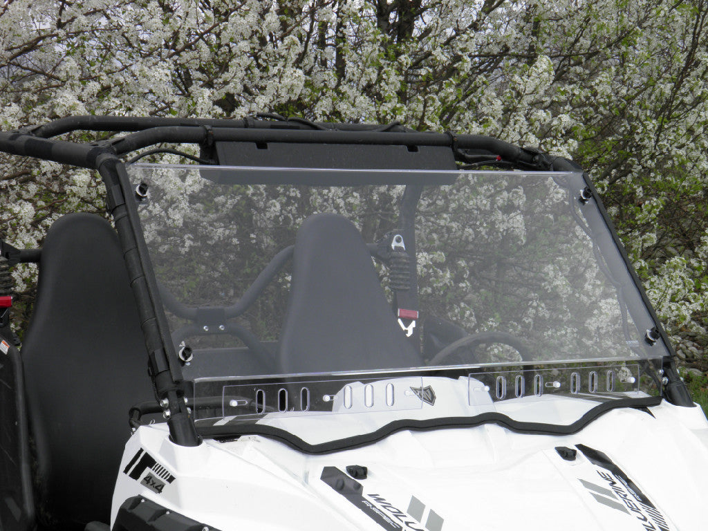 A Yamaha Wolverine R-Spec (2016-2018) with a 1 Pc. Lexan Windshield is parked by blossoming trees. The white off-road vehicle features two black bucket seats, safety harnesses, visible roll bars, and a windshield reflecting outdoor light.