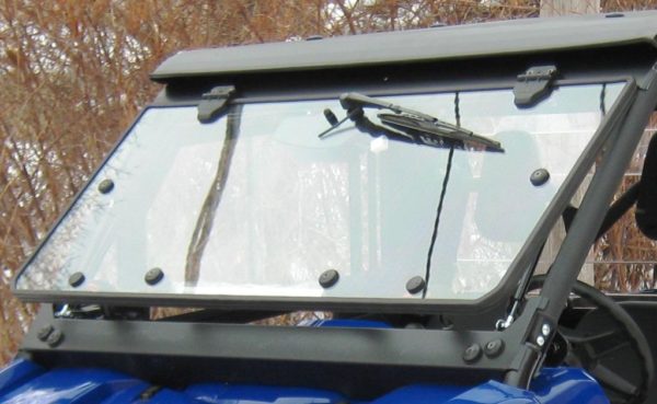 Close-up of the Wiper / Washer Kit – Polaris Ranger XP1000 mounted on a blue off-road vehicle’s transparent windshield, secured with black brackets and bolts; dry brown branches are blurred in the background.