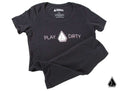 The Assault Industries 2021 Play Dirty Womens Tee is a black short-sleeve shirt featuring “PLAY DIRTY” in white and pink across the chest, separated by a geometric logo. The tee is shown laid flat on a white background with slight folds at one sleeve and 