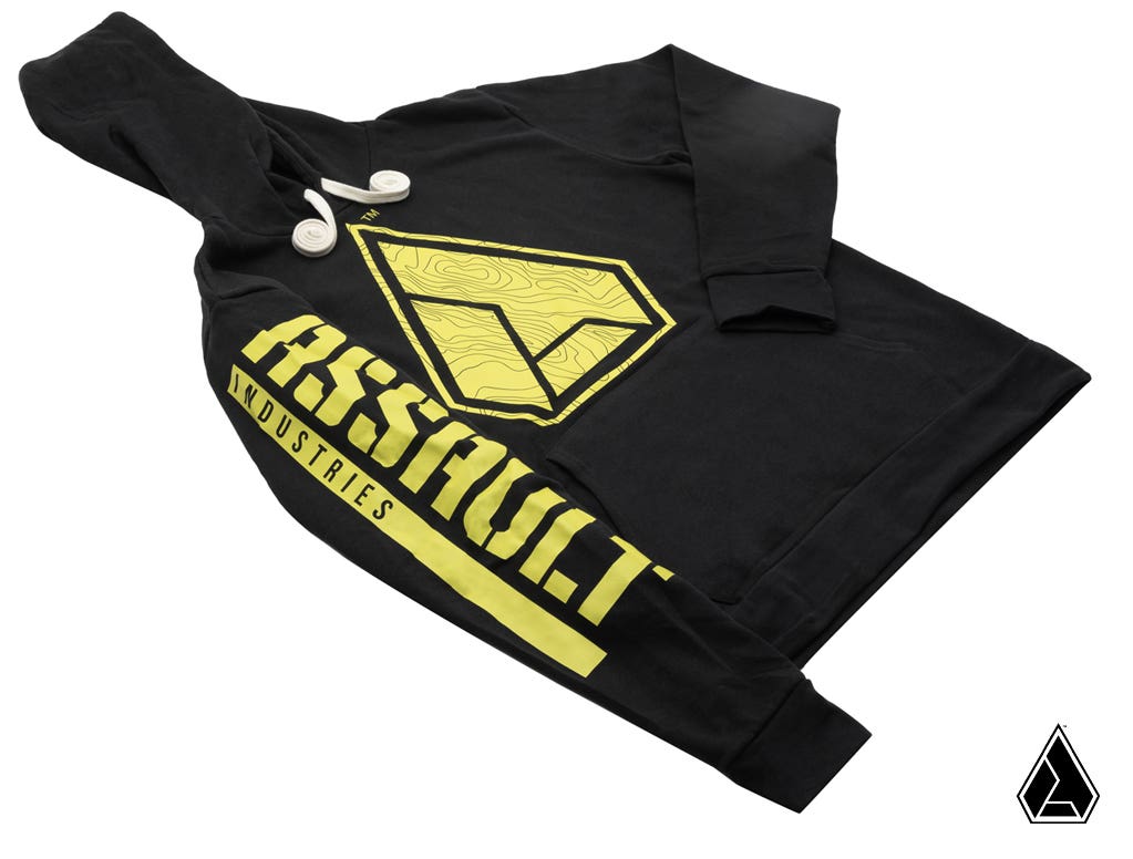 The Assault Industries Topographic Hoodie is black with white drawstrings, features large yellow ASSAULT INDUSTRIES text on the right sleeve, a bold yellow logo on the chest, and a small matching logo in the lower right corner.