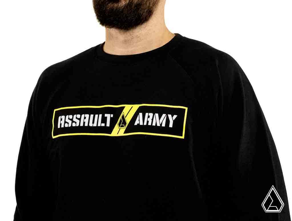 A bearded man wears the Assault Industries Army Sweatshirt, which has ASSAULT ARMY in bold white letters on a black and yellow background with triangular logos, set against a white backdrop.