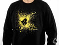 Someone wears the Assault Industries Impact Crewneck Sweatshirt, featuring a black base with a yellow splatter design and a stylized wolf head logo centered above small ASSAULT INDUSTRIES text. The wearer’s face is not visible.
