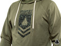 A person wears the Assault Industries Chevron Hoodie in olive green with white drawstrings, a geometric digital camo logo and ASSAULT on the chest, raglan sleeves, and a small white triangle logo at the bottom right.
