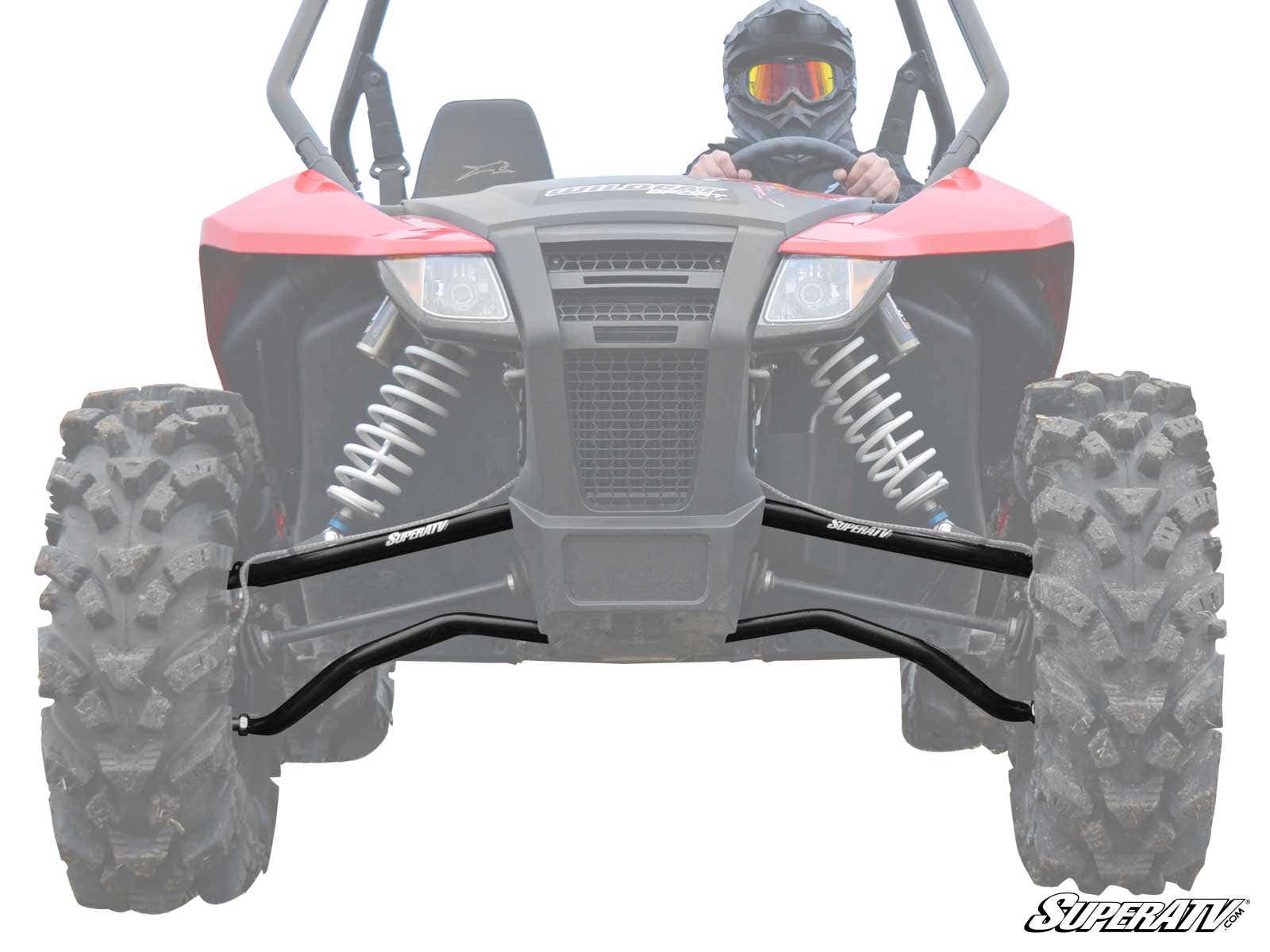 A red off-road ATV with large, rugged tires and exposed suspension is shown from the front. The driver wears a helmet and goggles. Two black Arctic Cat Wildcat Sport High Clearance A-Arms are attached to the front suspension, boosting durability and clear