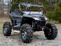 A person wearing a helmet drives a black Arctic Cat Wildcat Trail Sport Flip Windshield side-by-side ATV with aggressive off-road tires over rocky terrain, surrounded by trees and grass, highlighting its rugged, adventurous design.
