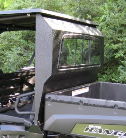 A close-up shows a black utility vehicle cab with textured sides and an Armor Tech Polaris Ranger Sliding Glass Rear Window, next to a gray cargo bed. Green foliage fills the background, with RANGER visible on the side.
