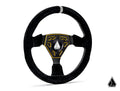 The Assault Industries Universal Navigator Suede UTV Steering Wheel features a black suede-like cover, yellow and black metal center with a triangular logo, accent stitching, a gray top marker, and a matching logo on the bottom right of the white backgrou