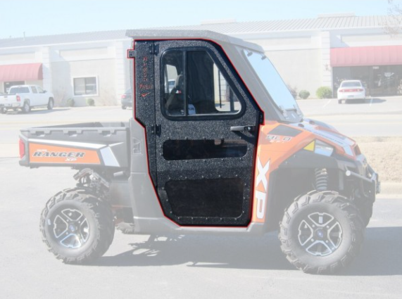 A side view of Full Steel Doors By Armor Tech, installed on a Polaris Ranger 570/500 (Mid-Size) with large off-road tires and a closed black-framed door, parked in a lot with vehicles and commercial buildings in the background.