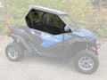 A CF Moto Z-Force 800-950 side-by-side with rugged tires and sporty graphics is parked on pavement, featuring the 2023+ Trail Vented Scratch Resistant Polycarbonate Upper Doors Kit (Tinted); greenery and a chain-link fence are in the background.