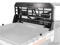 A Bobcat UV34 Headache Cargo Rack with horizontal slats is mounted at the front of a white and gray Bobcat utility vehicle’s bed, displaying the SuperATV logo; the empty bed reveals mounting bolts and side branding.