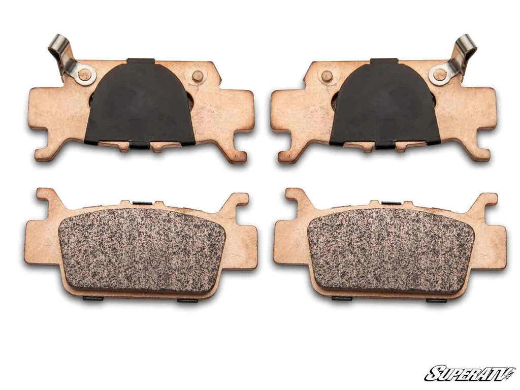 Four Honda Talon 1000 Sintered Brake Pads are arranged in two rows on a white background. The top row shows the backs with black sections and metal clips; the bottom row displays the textured friction surfaces. The SuperATV logo is visible in the corner.