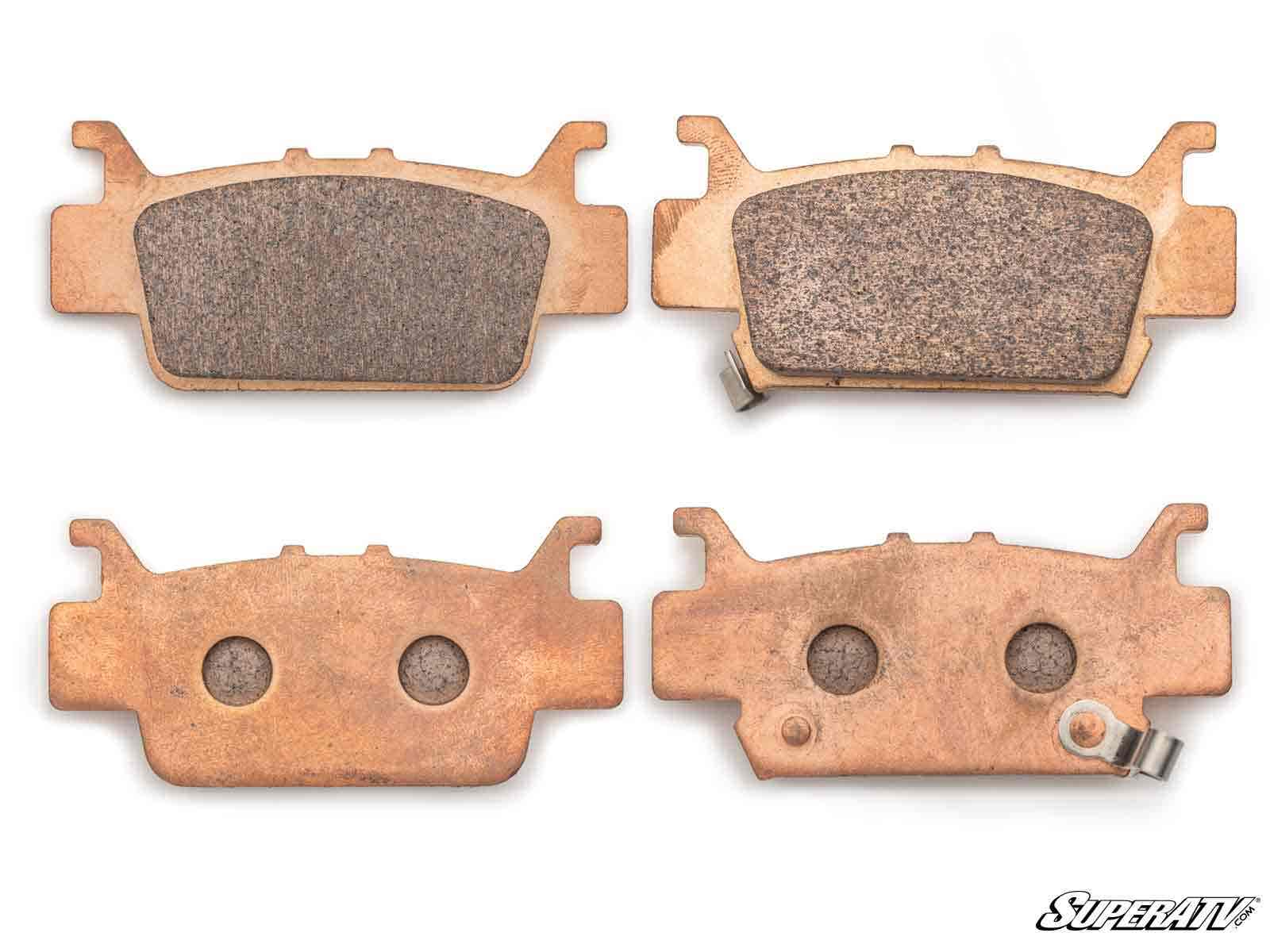 Four Honda Pioneer 1000 Sintered Brake Pads are shown, two face up showing friction surfaces and two face down revealing metal backing plates, one with a clip. The SuperATV logo appears in the bottom right corner.