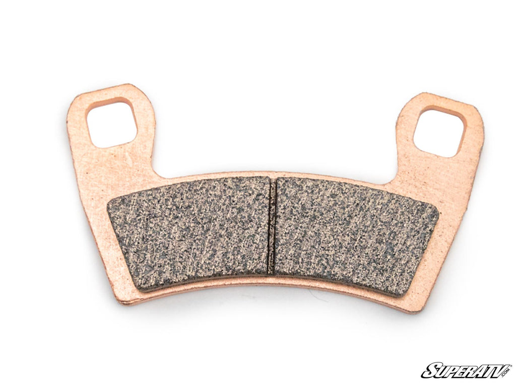 A single Polaris General Brake Pad, copper-colored with two rectangular friction surfaces and two mounting holes, is shown on a white background. “SuperATV” appears in stylized text in the lower right corner.