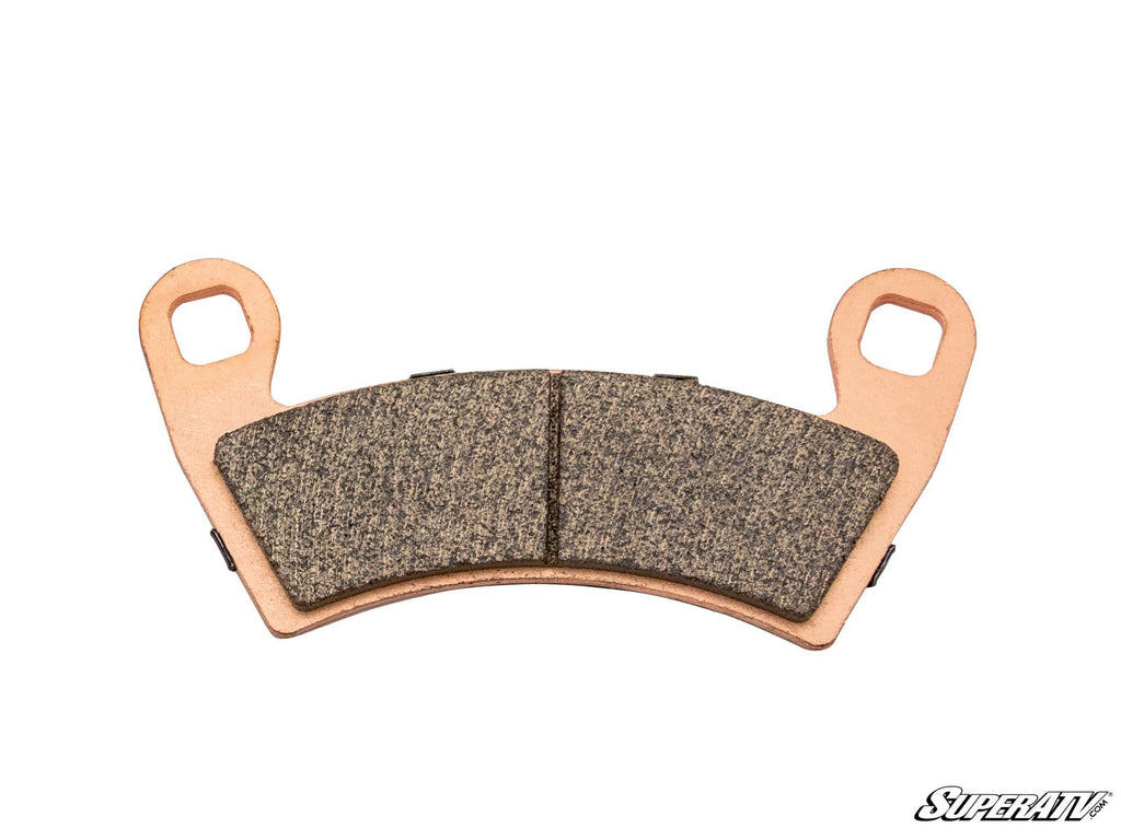 A single Polaris ATV Brake Pad featuring two mounting holes on each end, a textured dark friction surface, and a copper-colored backing plate. The SuperATV logo is visible in the lower right on a plain white background.