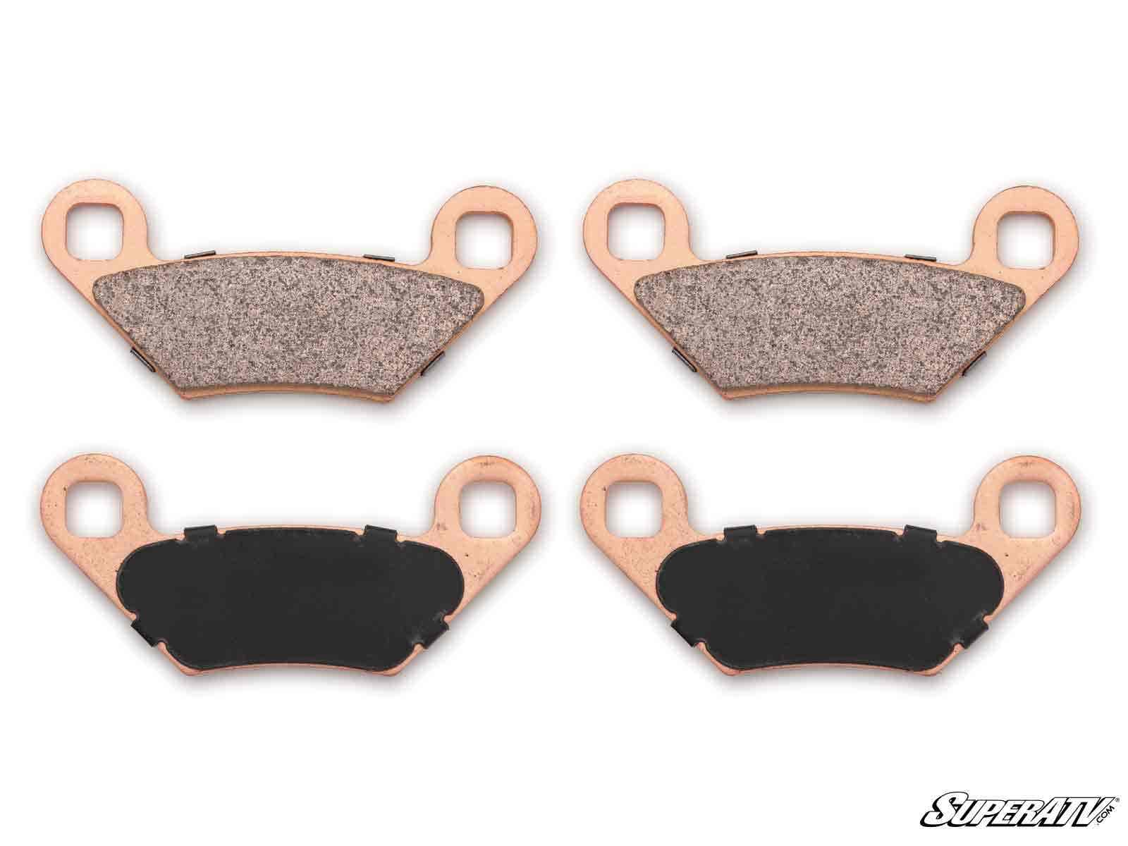 Four Polaris Sportsman Sintered Brake Pads are arranged on a white background in two rows. Each pad features copper-colored metal backing; the top pair has gray friction surfaces and the bottom pair has black ones. SuperATV appears in the lower right corn