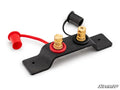 The Battery Terminals Relocation Kit includes a black rectangular mounting bracket with two brass terminals: one with a red ring and cap (positive) and one with a black ring and cap (negative), each with wire-attached covers. SuperATV logo at lower right.