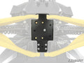 Close-up of a black Can-Am Maverick R Frame Stiffener installed under an off-road vehicle. Yellow suspension arms, springs, and bolts are visible. The background is faded, with the SuperATV logo in the bottom right corner.