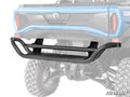 A Can-Am Commander 1000 Rear Bumper made of black tubular steel with a step is installed on the back of a blue off-road vehicle with lifted suspension and large tires. The SuperATV logo appears at the bottom right. Background is white.