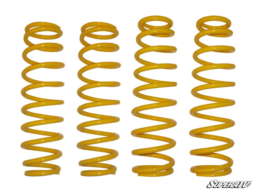 Four yellow, coiled metal springs of varying heights and tightness, from the Can-Am Commander 6 Lift Kit Replacement Springs (Set Of 4 Springs), are arranged upright in a row on a white background. The SuperATV logo appears in the bottom right corner.