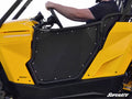 A person in a black shirt drives a bright yellow off-road vehicle equipped with Can-Am Commander Aluminum Doors. The vehicle features the SuperATV logo at the bottom right, with part of the steering wheel and dashboard visible.
