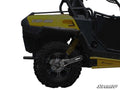 Close-up side view of a yellow and black Can-Am off-road vehicle highlighting the Can-Am Commander Extended Rear Trailing Arms by SuperATV, coil spring suspension, rugged rear wheel tread, and part of the branded black chassis.