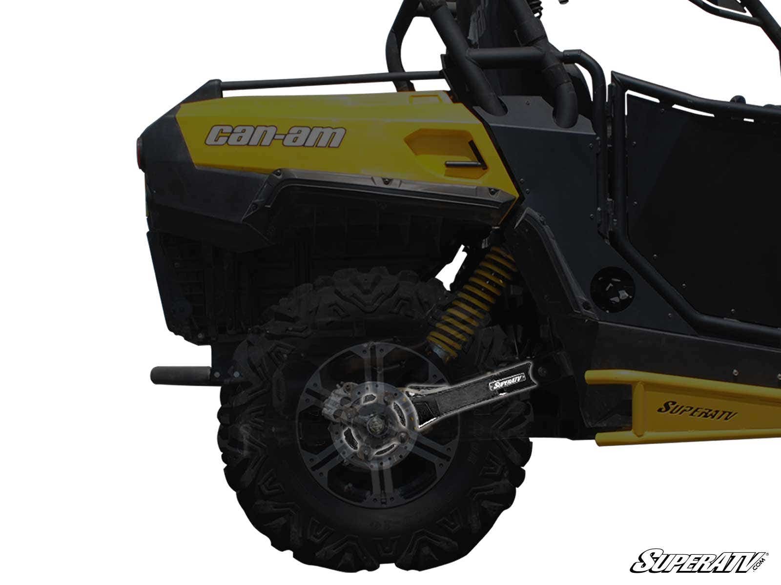 Close-up side view of a yellow and black Can-Am off-road vehicle highlighting the Can-Am Commander Extended Rear Trailing Arms by SuperATV, coil spring suspension, rugged rear wheel tread, and part of the branded black chassis.
