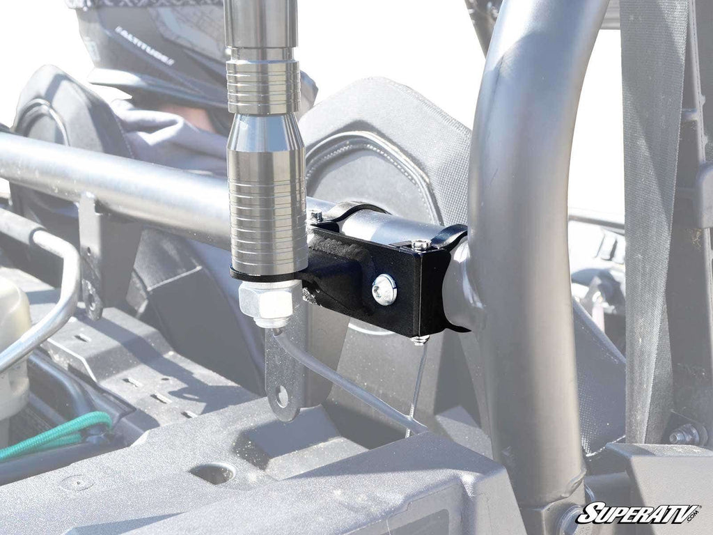 A close-up shows Whip Light Mounting Brackets securing a whip light upright to an off-road vehicle’s roll cage with bolts. Parts of the interior and frame are visible, with the SuperATV logo in the lower right corner.