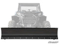 A Can-Am Commander Plow Pro Snow Plow, in black metal, is mounted to the front of a rugged-tired UTV. The UTV is partially faded to highlight the plow, with the SuperATV logo visible in the bottom right corner.