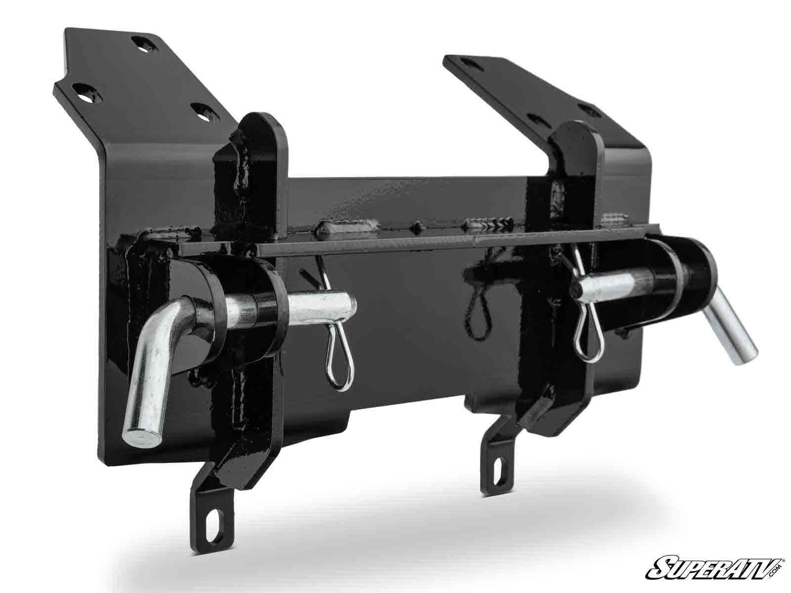 The Can-Am Commander 1000 Plow Pro Snow Plow Mount is a black metal bracket with two large cotter pins and rods, multiple bolt holes for mounting, a glossy finish, and the SuperATV logo in the bottom right corner.