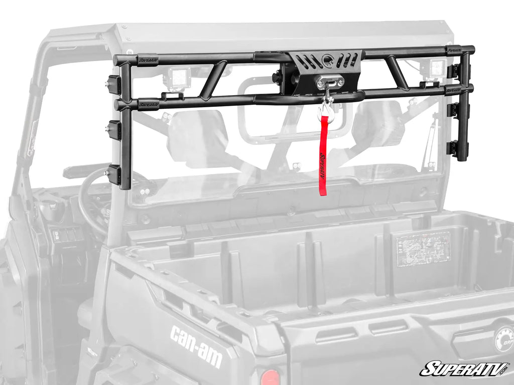 The Can-Am Defender Game Loader Rack, a black metal winch mount with a red synthetic winch rope, is installed across the cargo bed of a gray Can-Am side-by-side. The rack is shown in full color; SuperATV logo appears at the bottom right.