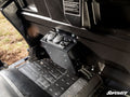 A Can-Am Defender Cab Heater is mounted on the floor behind the front seats. It has two round control dials, two air vents, black textured floor mats nearby, molded black panels, and displays the SuperATV logo.