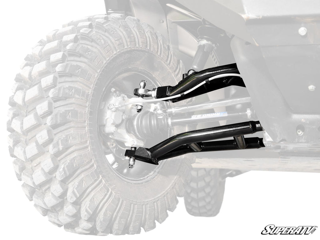 Close-up of Can-Am Defender HD10 Atlas Pro Heim Joint 1.5 Forward Offset A-Arms and black axles connected to a rugged tire; vehicle body faded to highlight the suspension, with the “SuperATV” logo at bottom right.