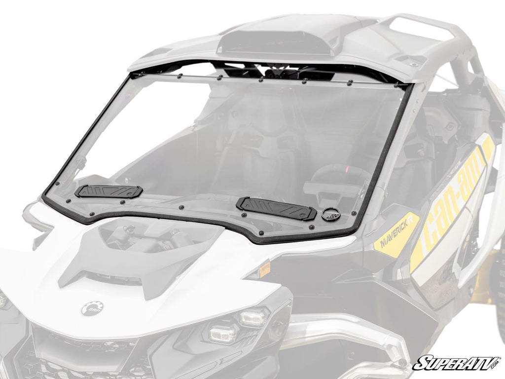 A Can-Am Maverick R Vented Full Windshield with a black frame and vents is installed on a white and yellow Can-Am Maverick side-by-side, set against a white background. The SuperATV logo is in the bottom right corner, highlighting the windshield.