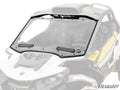A Can-Am Maverick R Vented Full Windshield with a black frame and vents is installed on a white and yellow Can-Am Maverick side-by-side, set against a white background. The SuperATV logo is in the bottom right corner, highlighting the windshield.