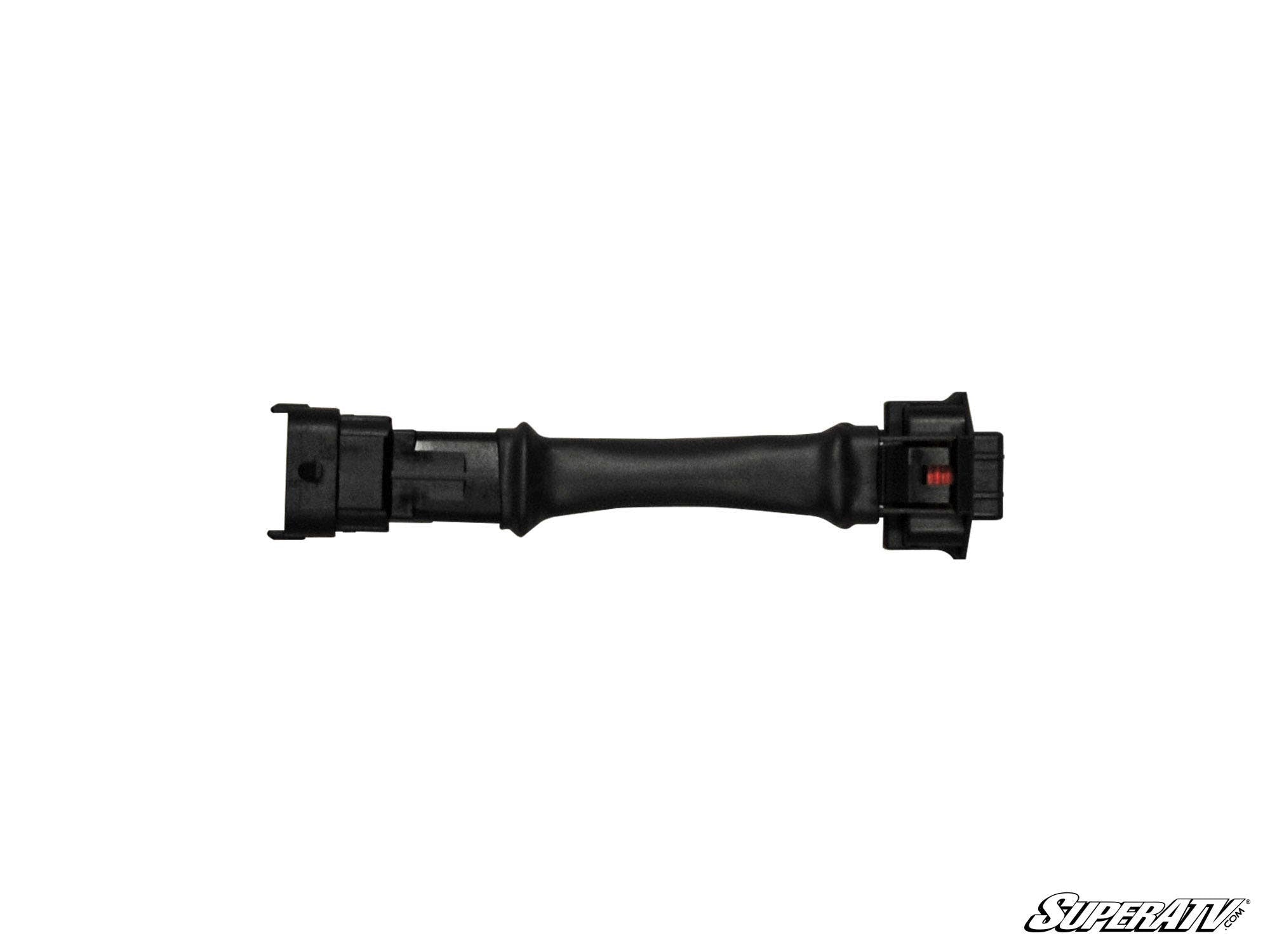 The Can-Am Commander Low Range Sport Mode Override is a black, flexible wiring harness adapter with rectangular connectors featuring visible slots and a red tab. The SuperATV logo appears in the bottom right corner against a white background.