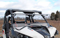 A white side-by-side with a Can-Am Maverick Flip Windshield and flat roof is parked on grass under partly cloudy skies, with 1000R on its front and leafless trees in the background.